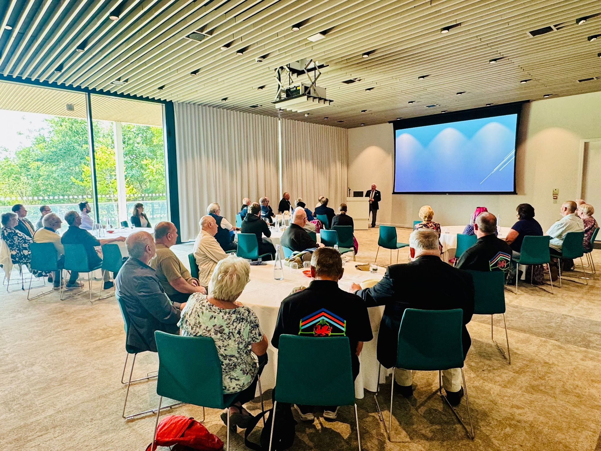 Photo of a room full of people, some in Armed Forces Uniforms, watching a presentation.